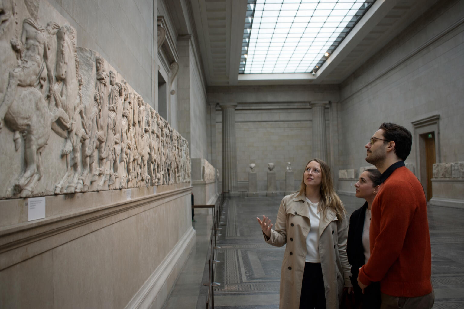 A photograph of a tour guide showing visitors around the British Museum, specifically around the Parthenon marbles, also known as Elgin marbles.